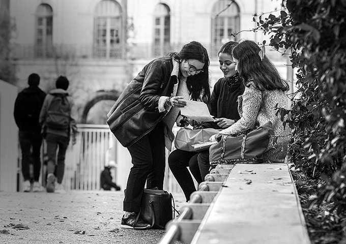 Sana, souriante, avec deux de ses amis dans la cour extérieure d'un lycée.