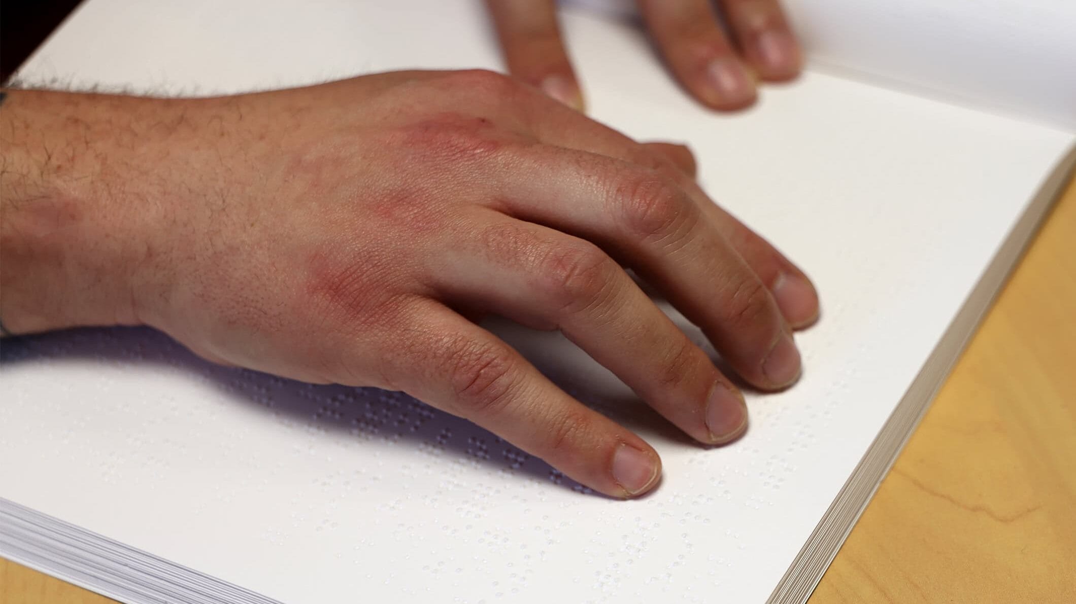 Photo zoomée sur une main qui lit un livre en braille.