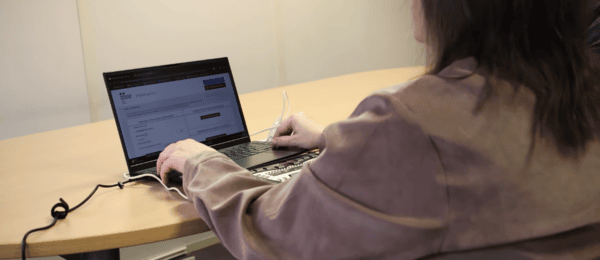 Photo d'une femme assise devant une table sur laquelle est posé un ordinateur et un pavé numérique. L'écran de l'ordinateur affiche le site internet des impôts.